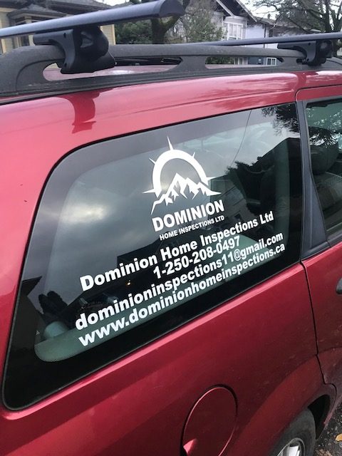 A red car's exterior with Dominion Home Inspections stickers on the windows.
