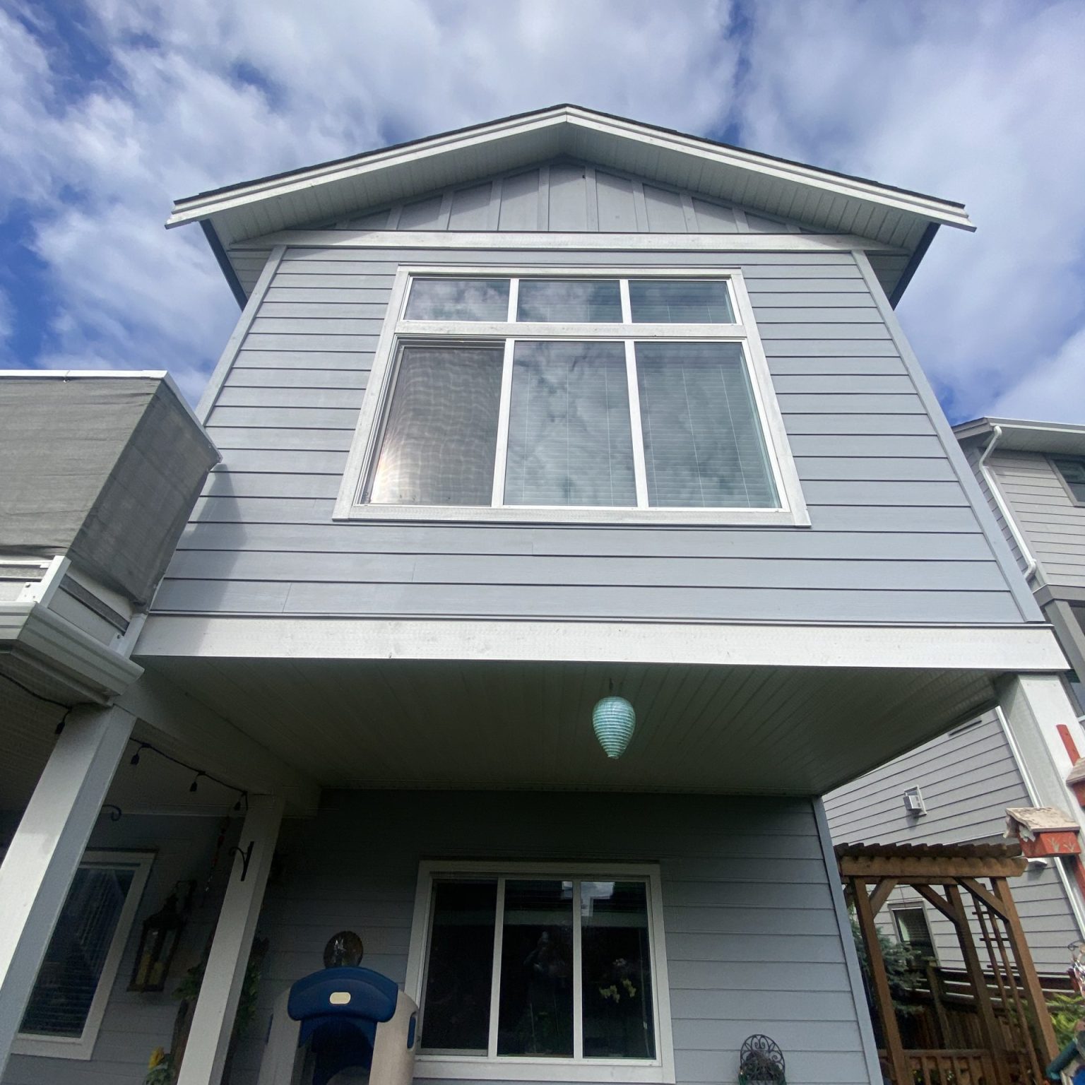A grey two-level home with white trim, looking up from the ground level up to the second level with clouds in the background.