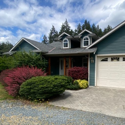 A teal house with a double garage and shrubbery out front.