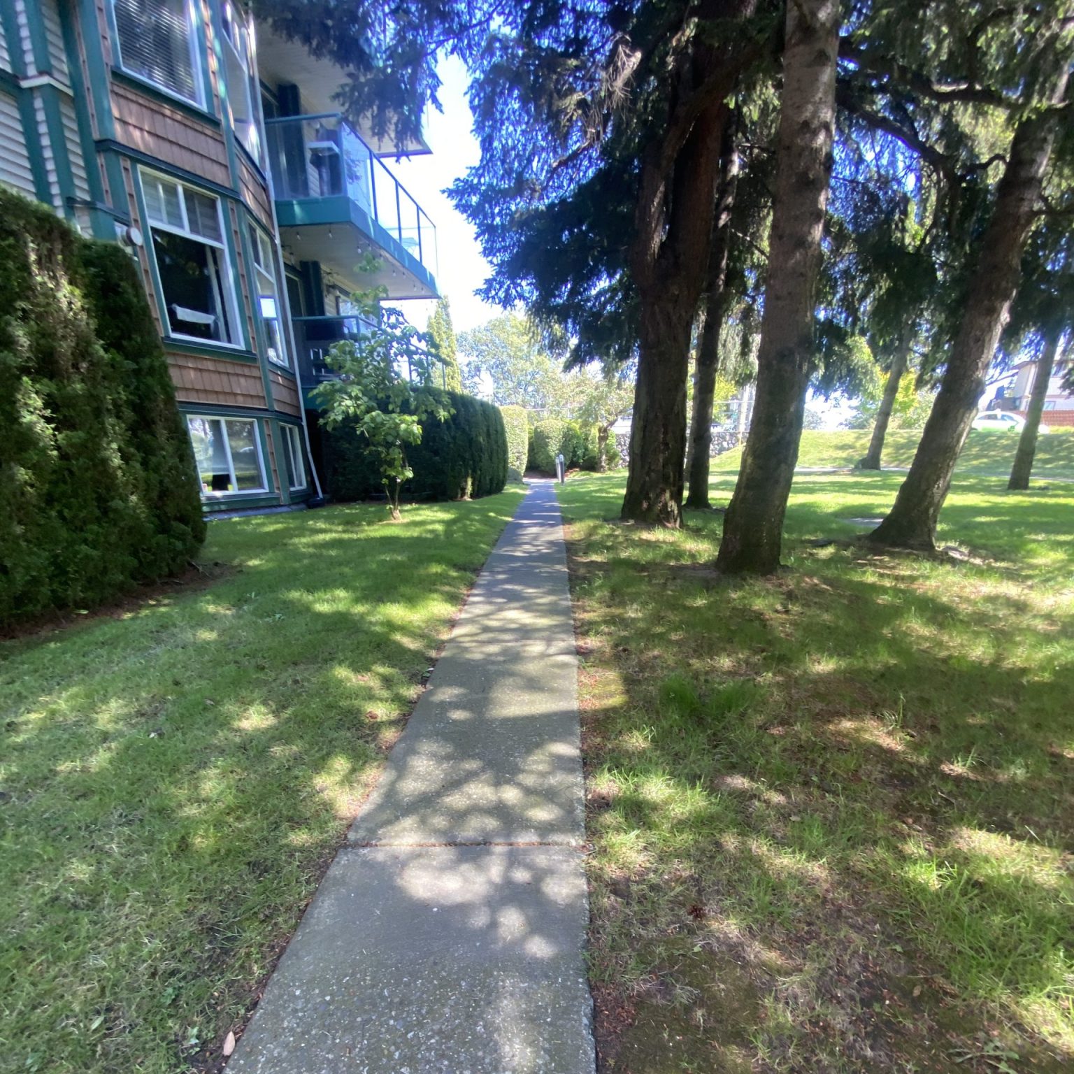 A sidewalk alongside a multi-family building with cream paint and green trim.