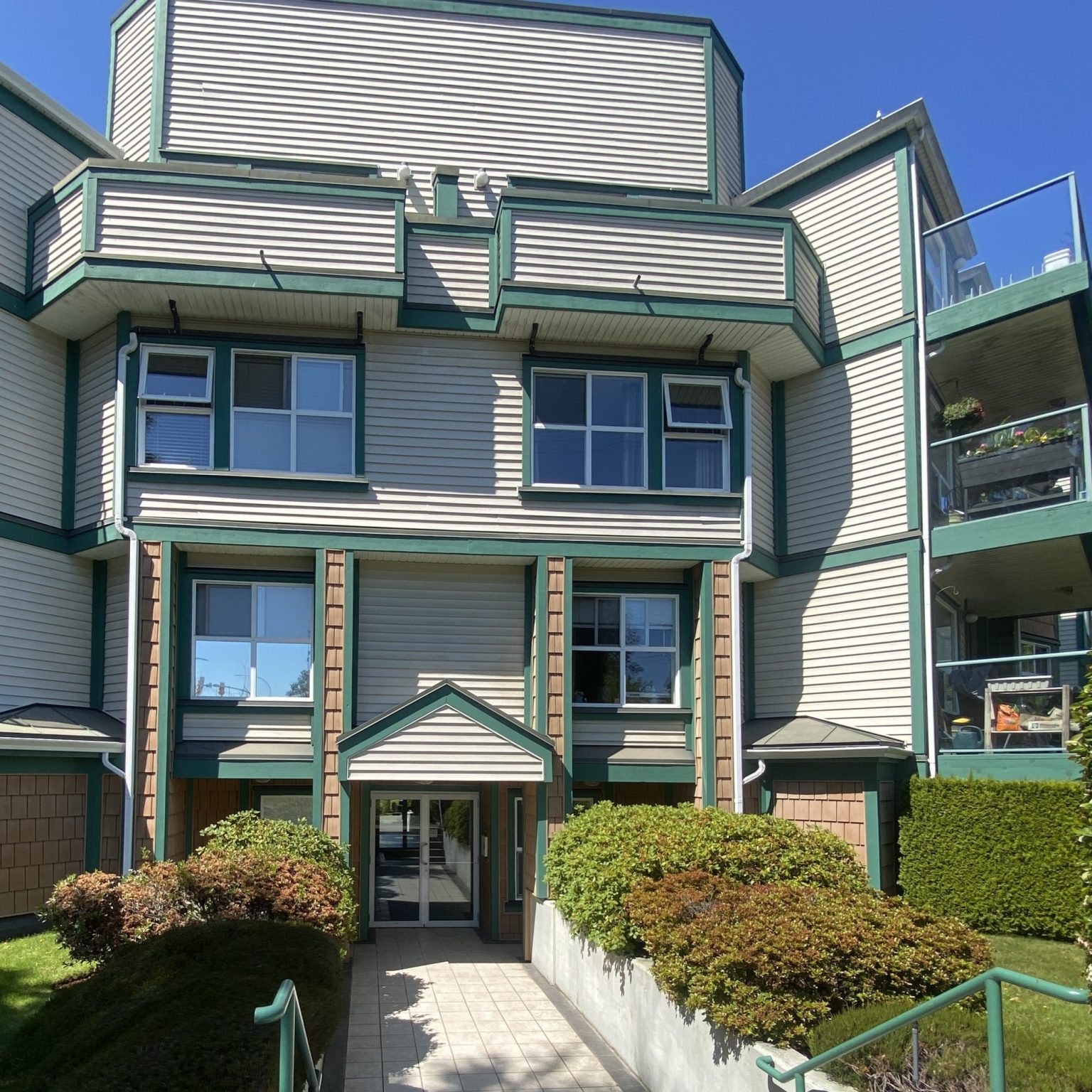 A multi-family building with three levels, cream paint and green trim, with glass patios.
