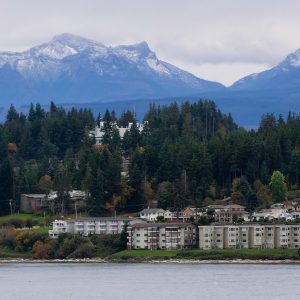 A view of Campbell River with some buildings along the ocean and trees and mountains in the background.