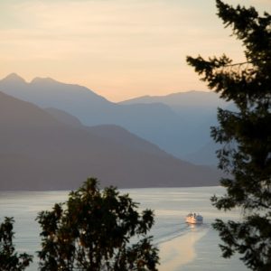 A view of a boat on the ocean with mountains in the background at sunset.